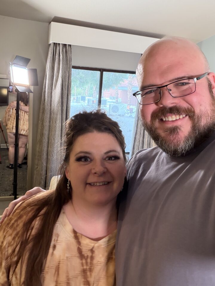 Sly Panorama behind-the-scenes selfie with a smiling collaborator beside a sunlit hotel window and ring light.