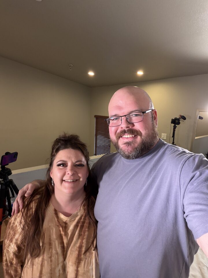 Sly Panorama behind-the-scenes selfie with a collaborator on a hotel film set with tripod and lighting visible behind them.