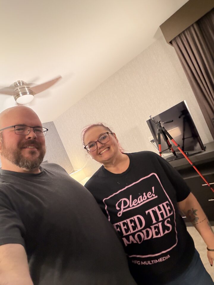 Sly Panorama hotel selfie with a smiling collaborator wearing a Please Feed The Models tee, ring light and tripod behind them.