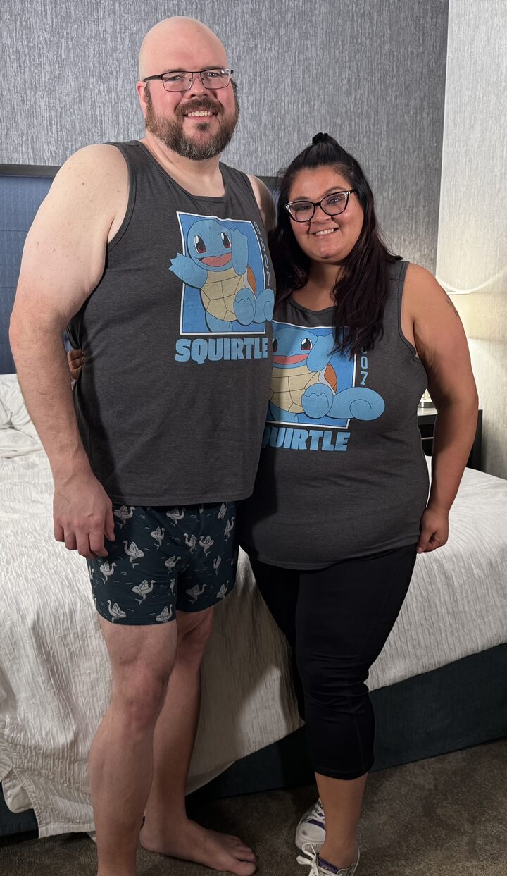 Sly Panorama and a smiling collaborator wearing matching Squirtle Pokemon tank tops in a hotel room.
