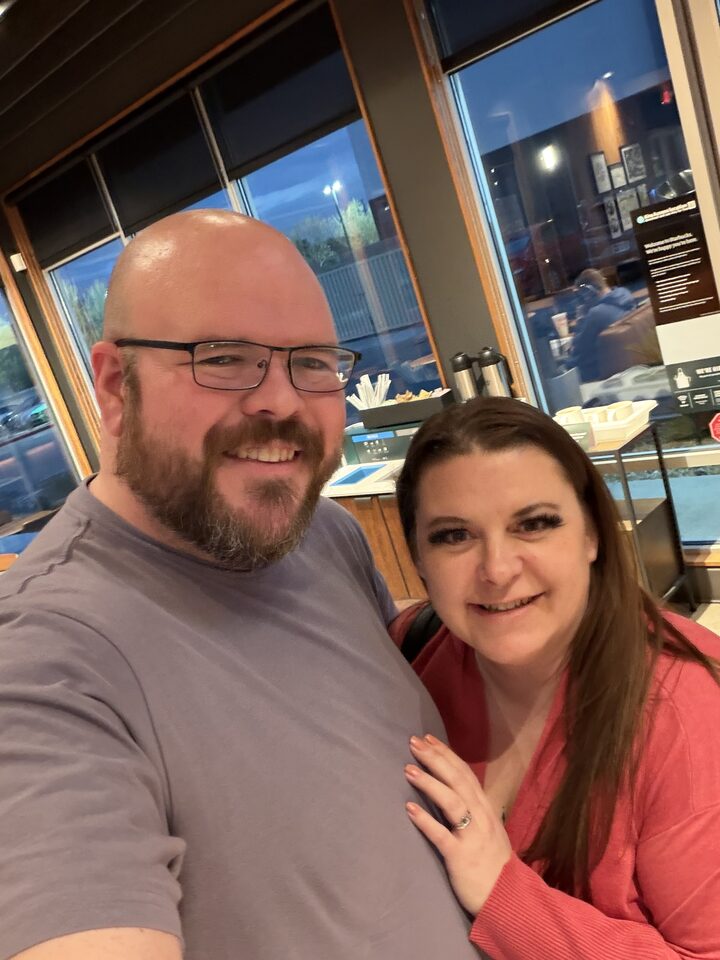 Sly Panorama selfie with a smiling collaborator at an evening restaurant with floor-to-ceiling windows.