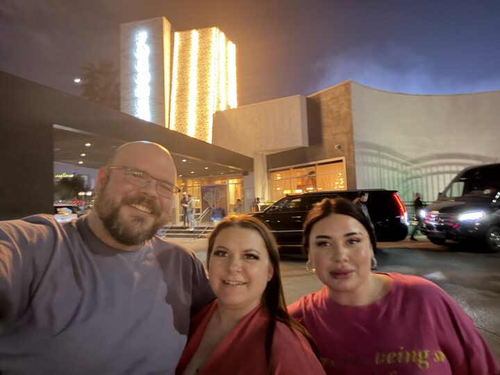 Sly Panorama nighttime Hollywood Boulevard selfie with two smiling collaborators in front of a lit hotel marquee.