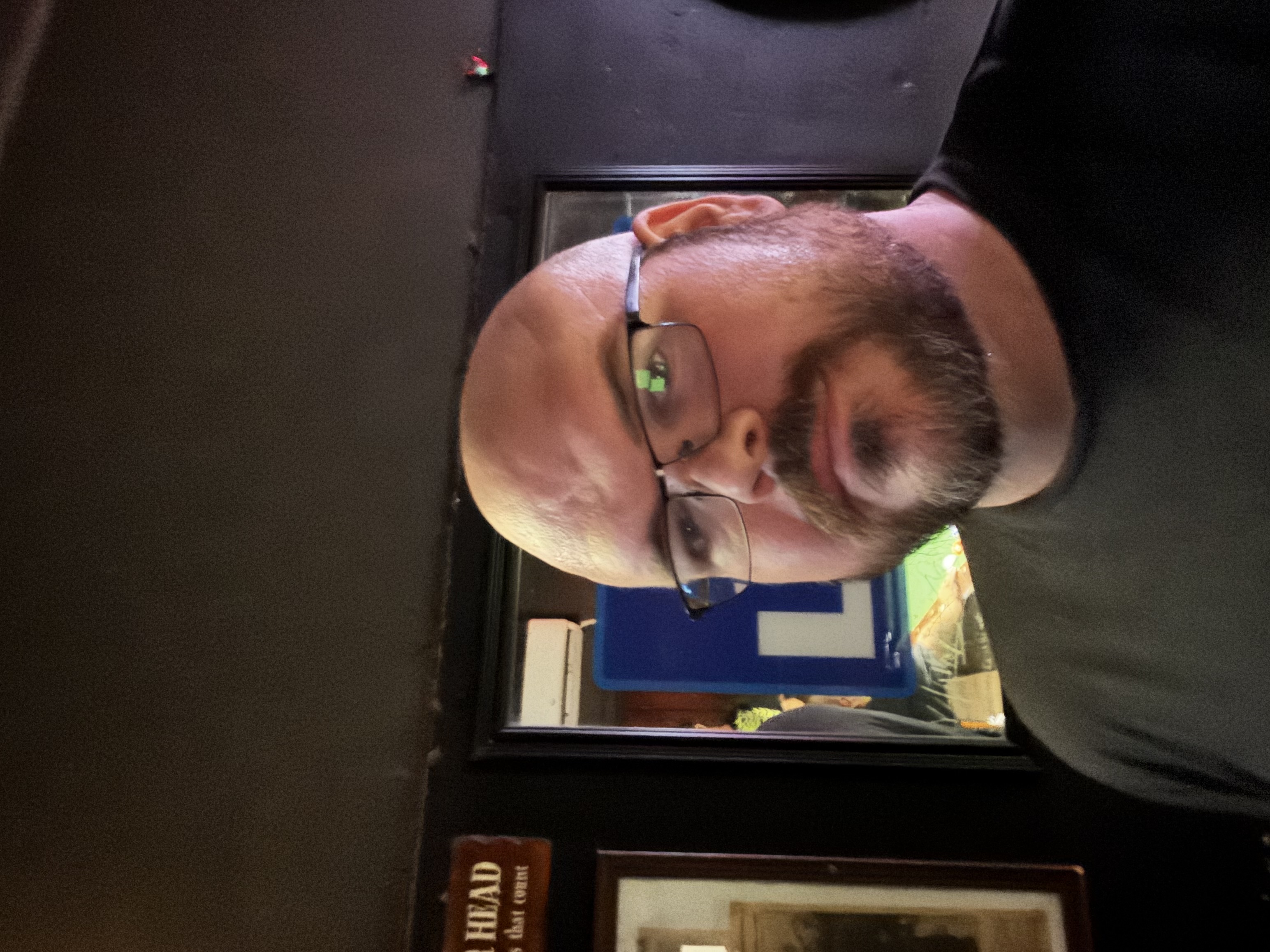 Sly Panorama portrait wearing glasses in a dim lounge with mirror reflections behind him.
