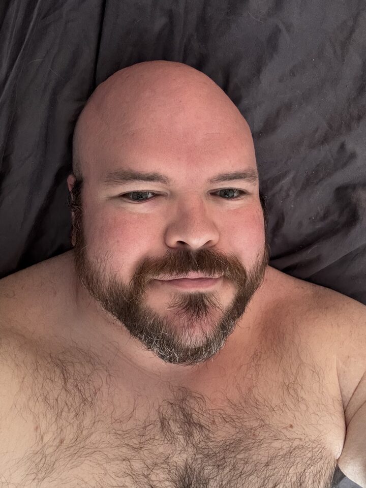 Sly Panorama shirtless close-up lying on charcoal grey bedding.