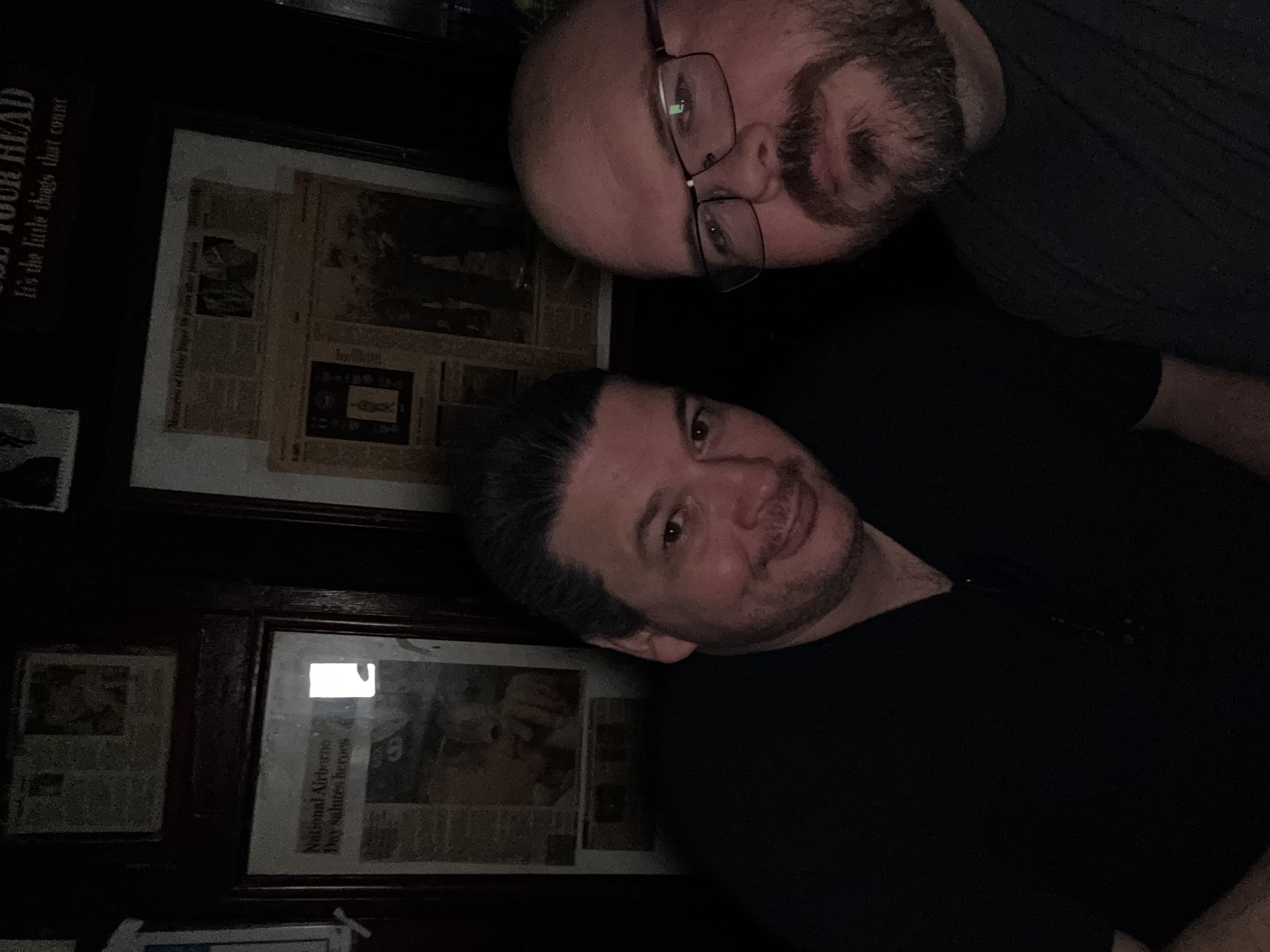 Sly Panorama selfie with a friend in a dim pub with framed memorabilia on the walls behind them.